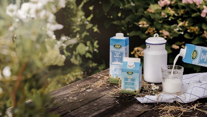Ziegenmilch in kleinem und großen Format auf Holztisch mit Milchkanne